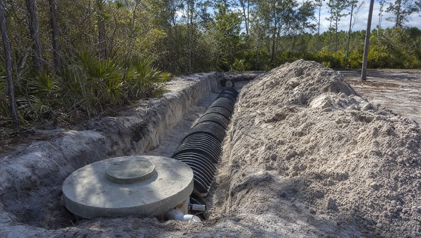 A new septic drain field going in on sandy North Florida ground, chamber sections laid in an open trench beside a concrete tank lid
